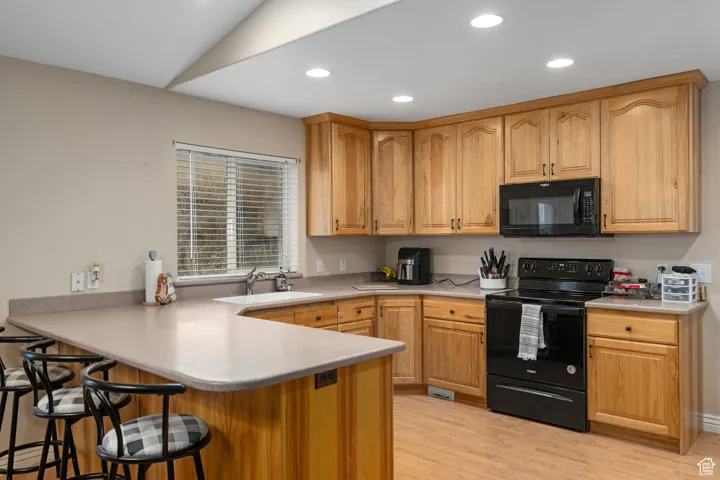 Kitchen with black appliances, a sink, a breakfast bar, a peninsula, and recessed lighting