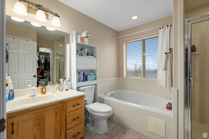 Bathroom featuring a tub with jets, vanity, a shower stall, toilet, and tile patterned floors