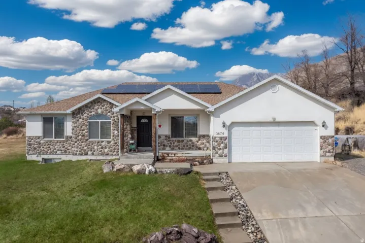 Ranch-style house with an attached garage, driveway, stone siding, and a front yard