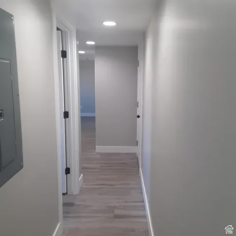 Corridor featuring baseboards, wood finished floors, recessed lighting, and electric panel