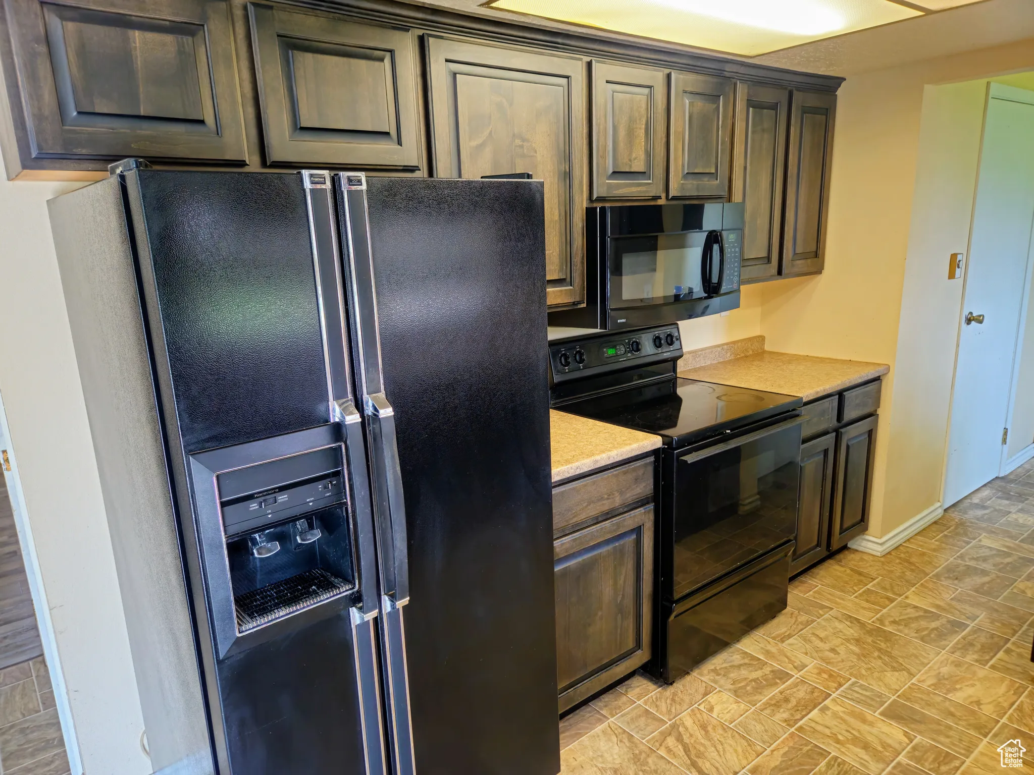 Kitchen featuring black appliances, light countertops, baseboards, and dark brown cabinetry