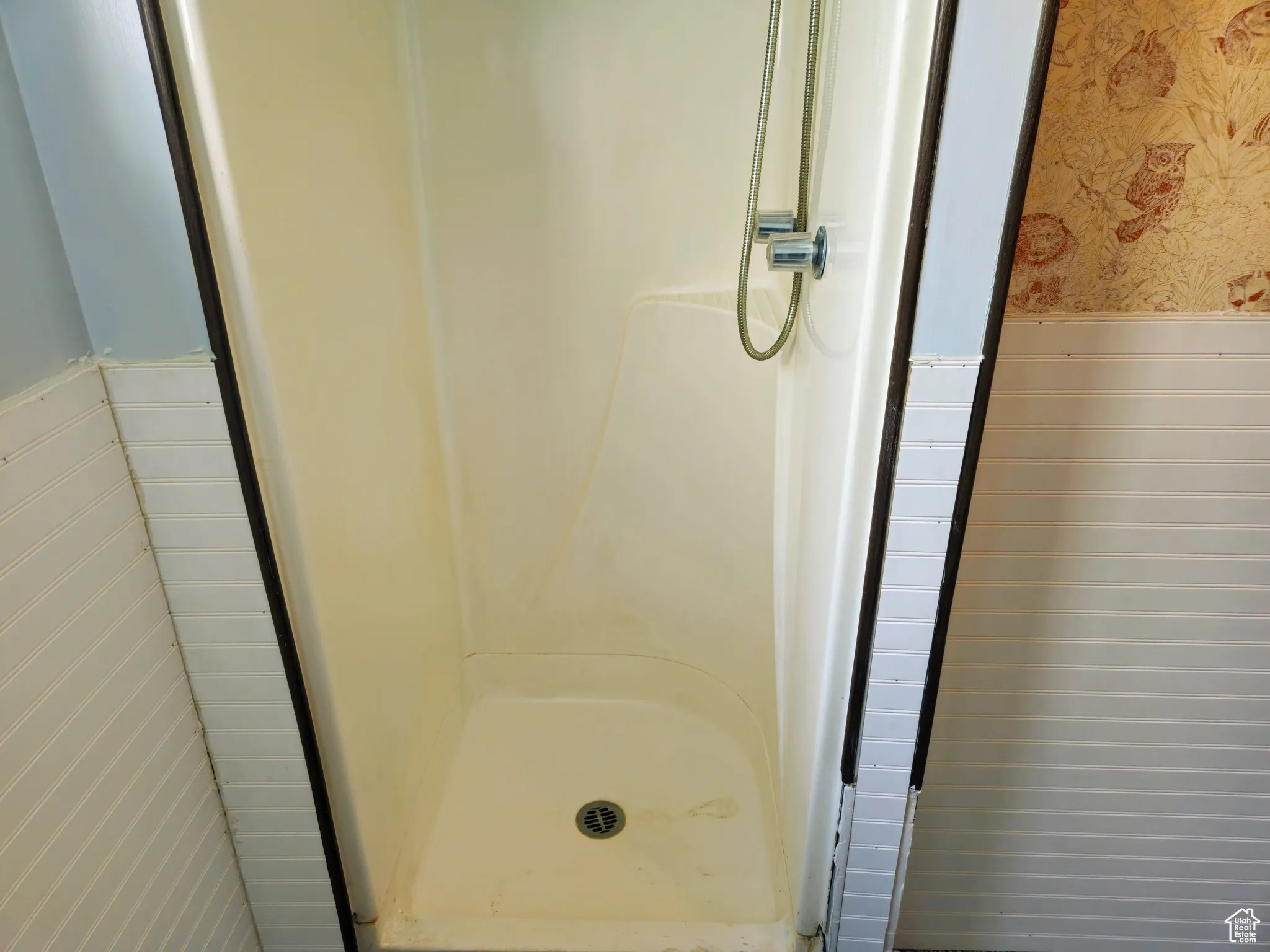 Bathroom with wallpapered walls, a wainscoted wall, and a shower stall