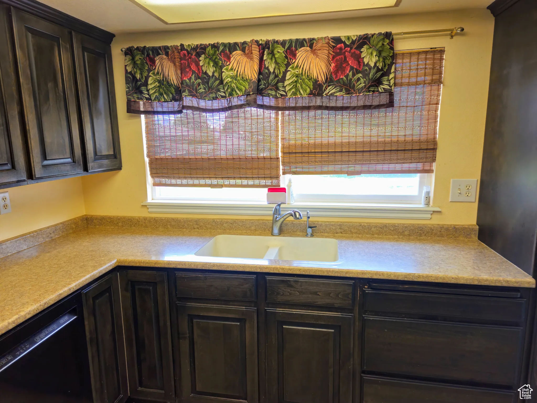 Kitchen with a sink, dishwasher, light countertops, and dark brown cabinets