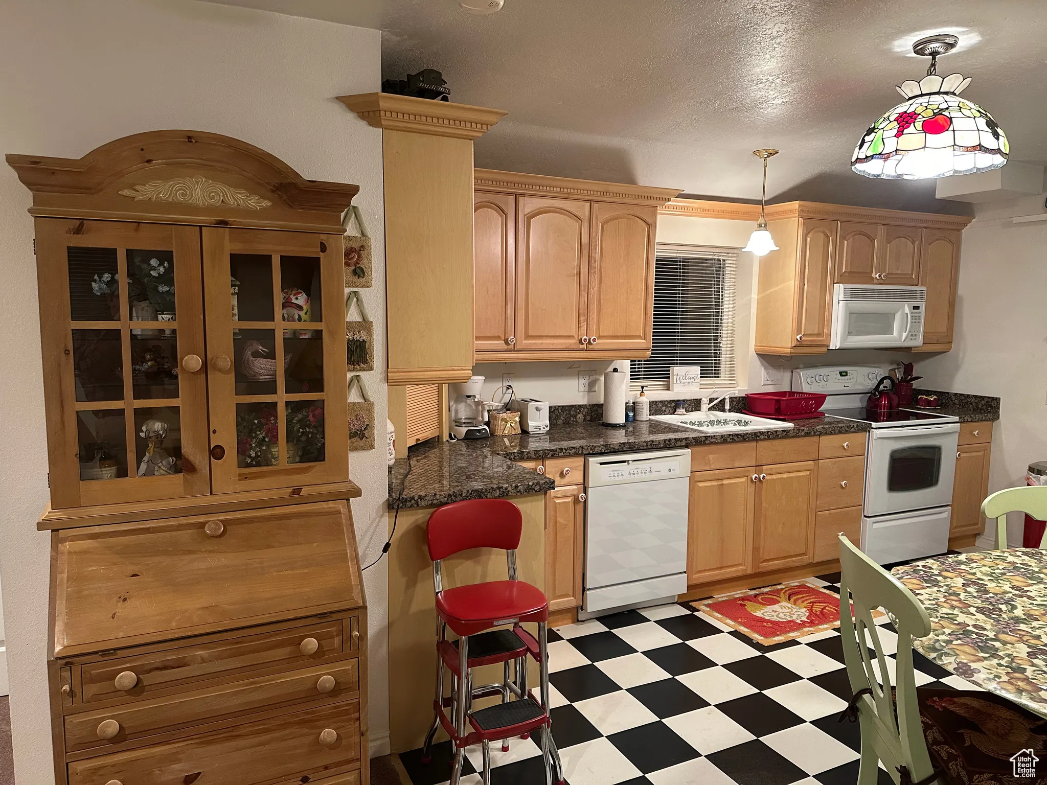 Kitchen featuring white appliances, light floors, a sink, dark countertops, and decorative light fixtures