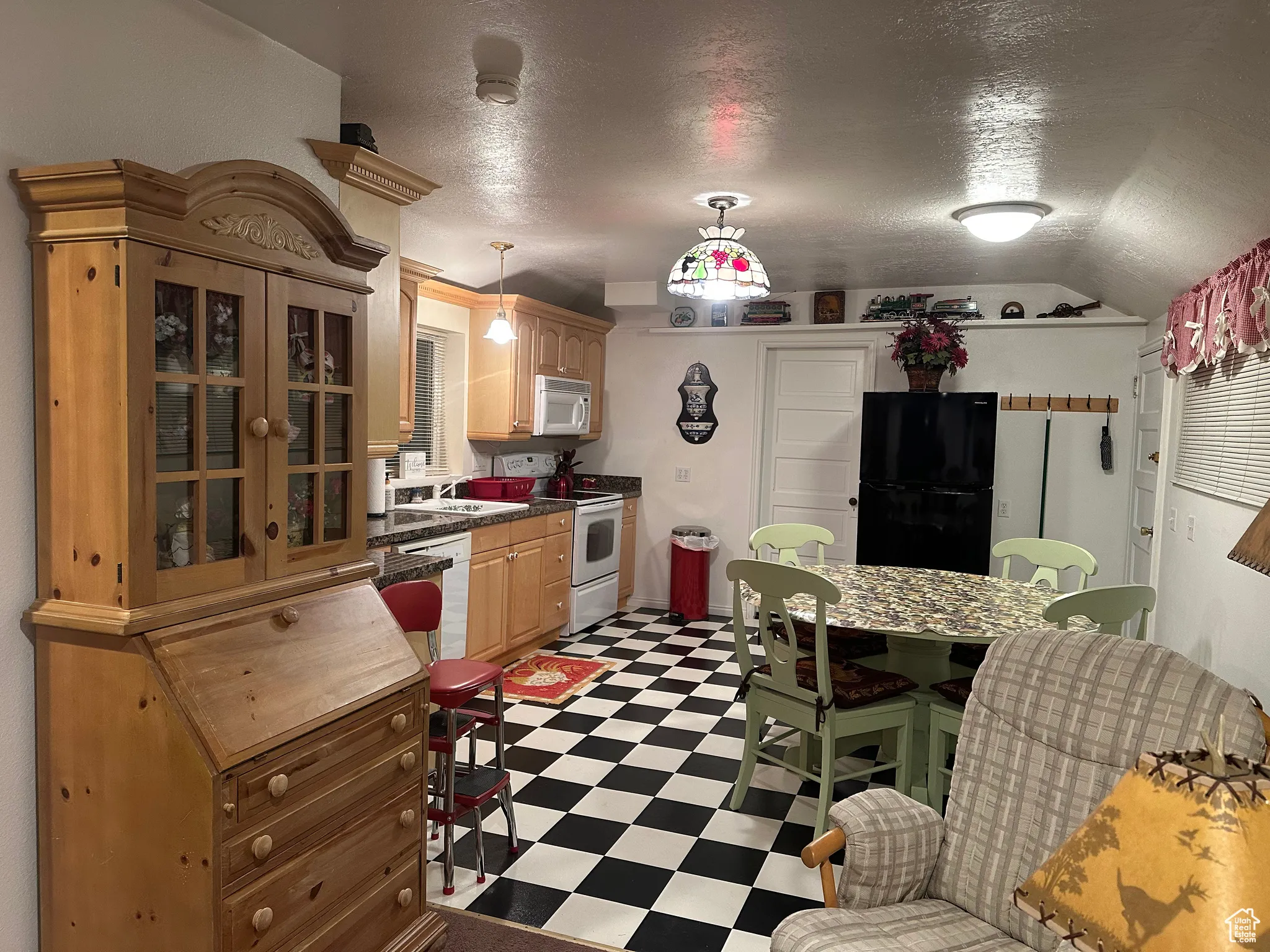 Kitchen with white appliances, light floors, a textured ceiling, vaulted ceiling, and decorative light fixtures