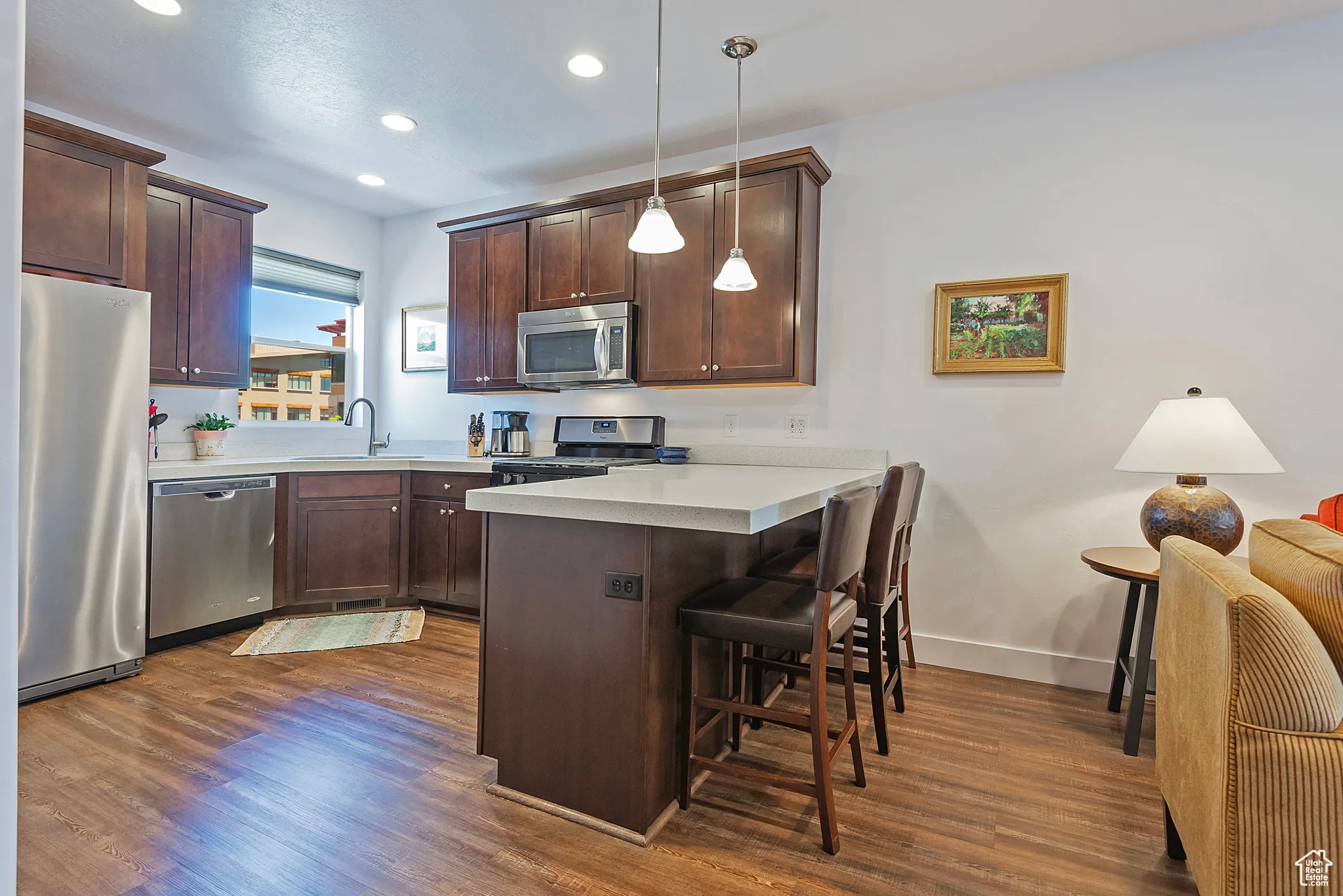 Kitchen with stainless steel appliances, a  kitchen breakfast bar, dark wood-style floors, and recessed lighting