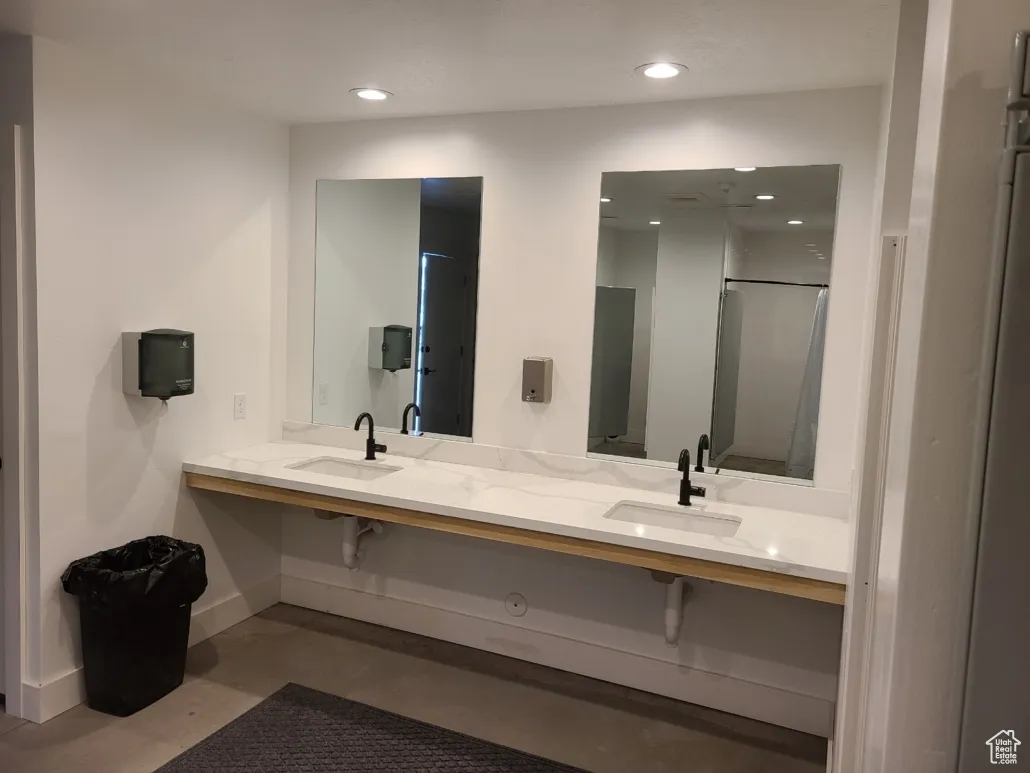 Bathroom with baseboards, recessed lighting, finished concrete floors, double vanity, and a shower with shower door