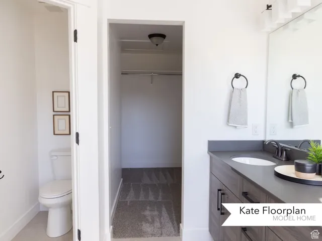 Full bathroom featuring vanity, toilet, a spacious closet, and baseboards