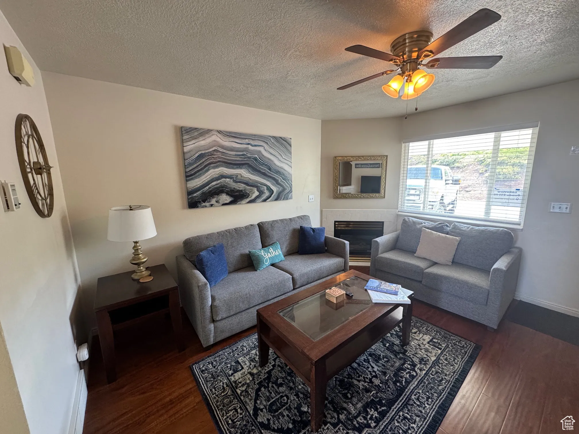 Living area featuring a textured ceiling, wood finished floors, ceiling fan, baseboards, and a tile fireplace