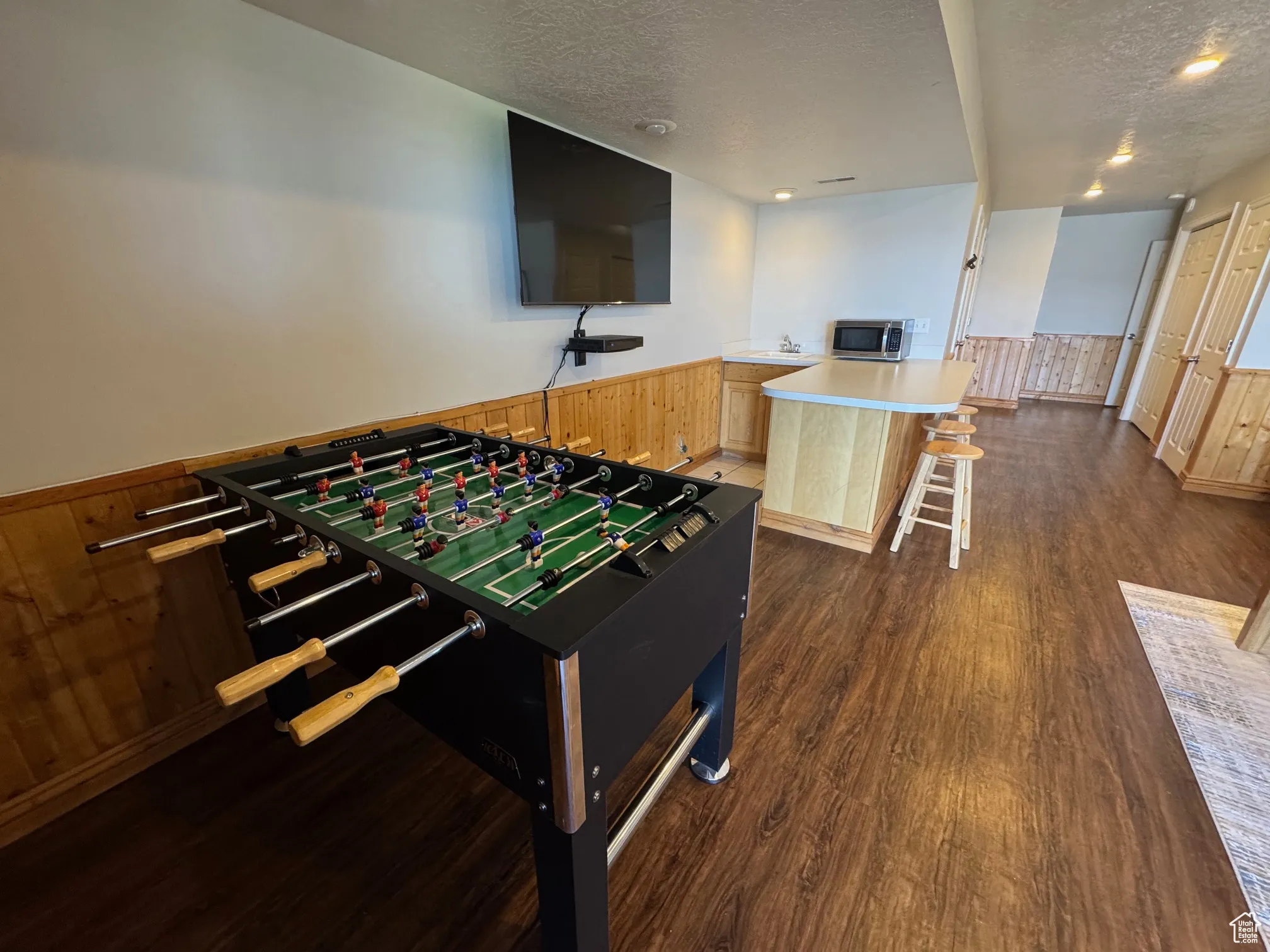 Game room with a textured ceiling, dark wood-style flooring, a wainscoted wall, a sink, and recessed lighting