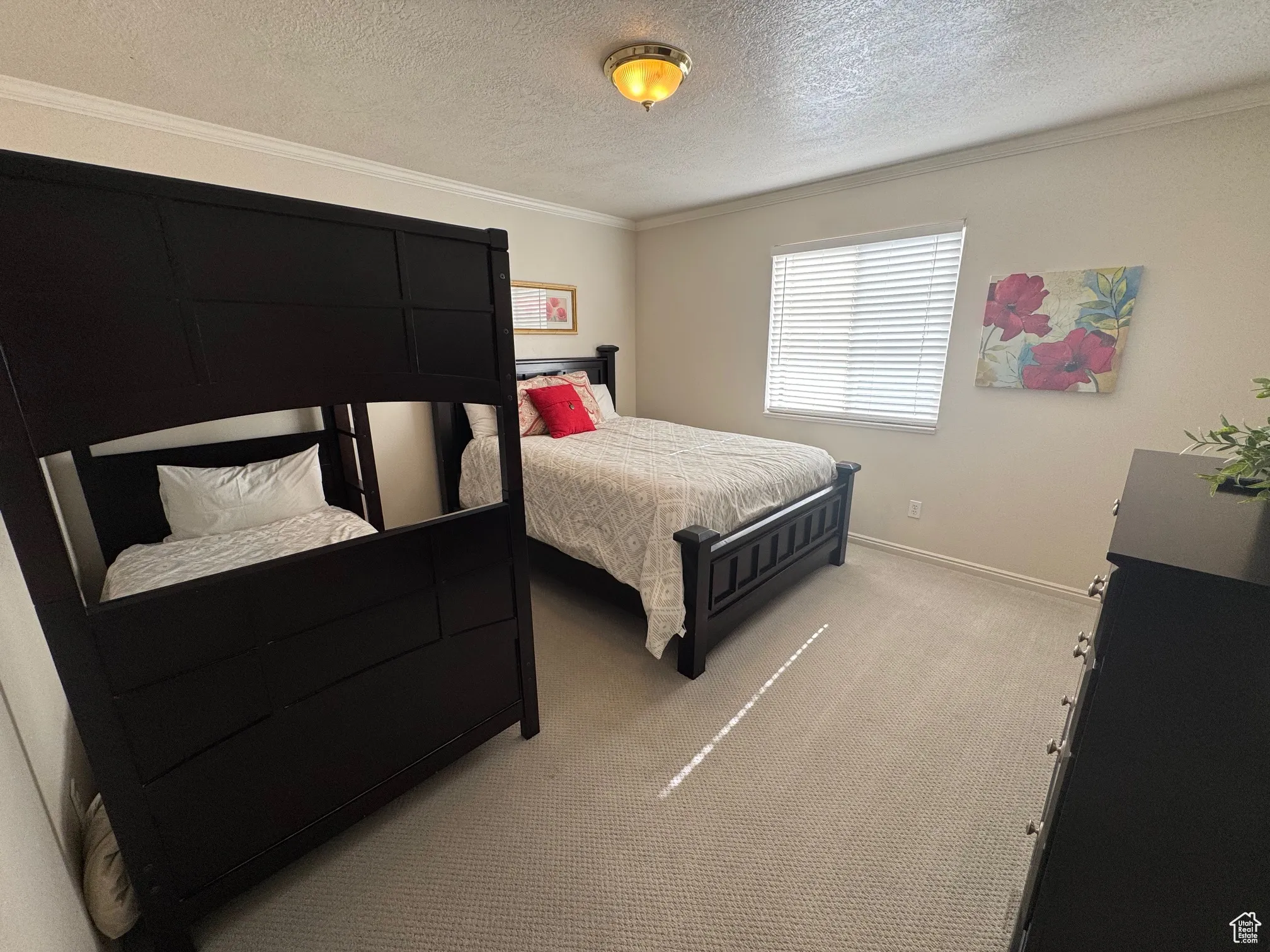 Bedroom featuring a textured ceiling, ornamental molding, light colored carpet, and baseboards