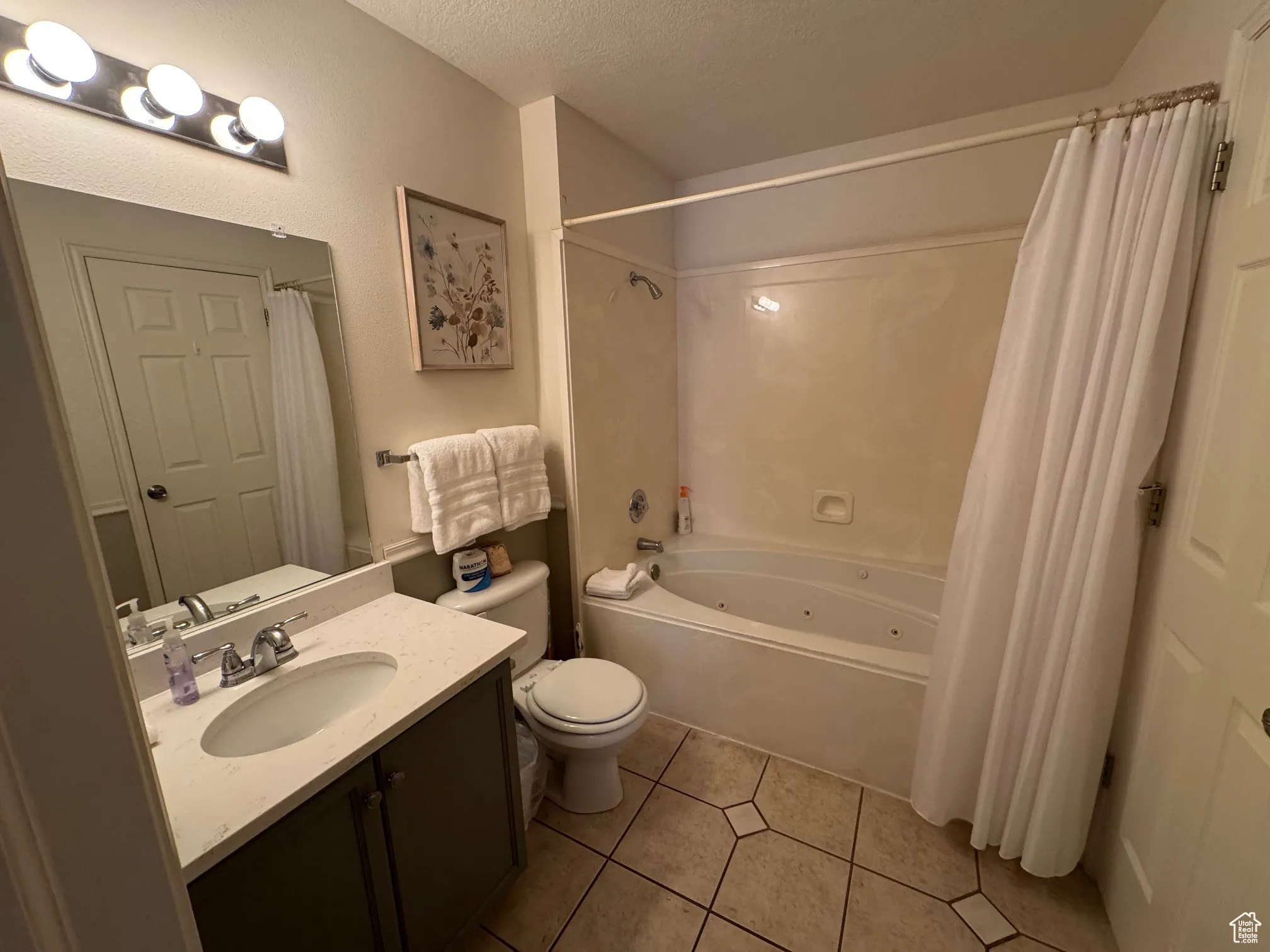 Full bath featuring toilet, shower / bath combo with shower curtain, vanity, a textured ceiling, and tile patterned flooring