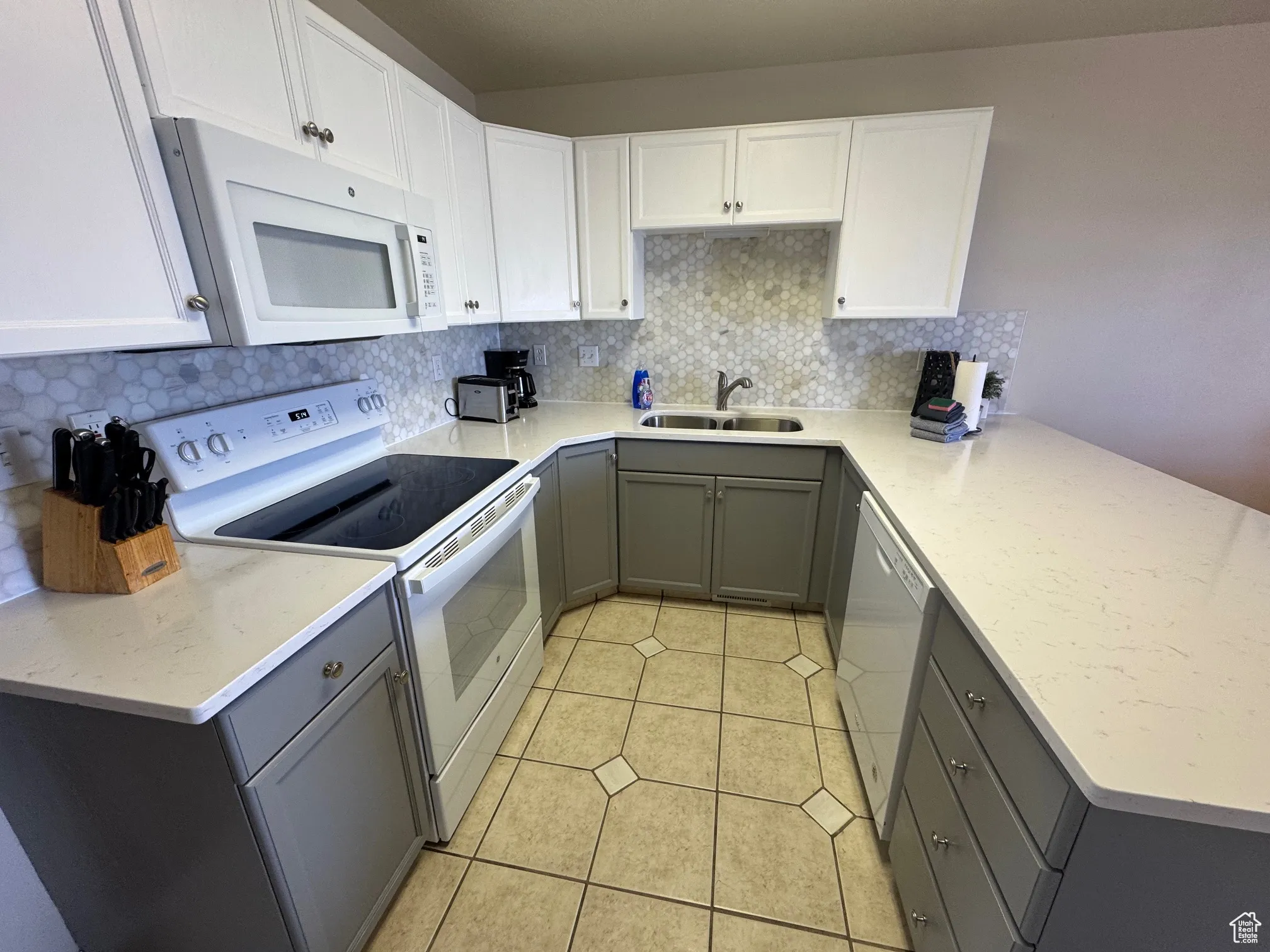 Kitchen featuring white appliances, gray cabinetry, a sink, a peninsula, and tasteful backsplash