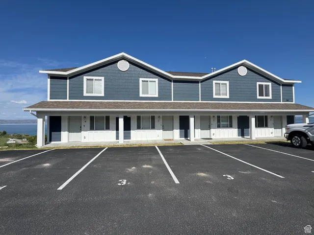 Townhome / multi-family property featuring uncovered parking, covered porch, and a shingled roof