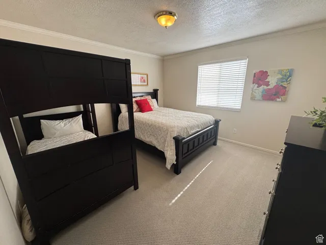 Bedroom featuring a textured ceiling, ornamental molding, light colored carpet, and baseboards