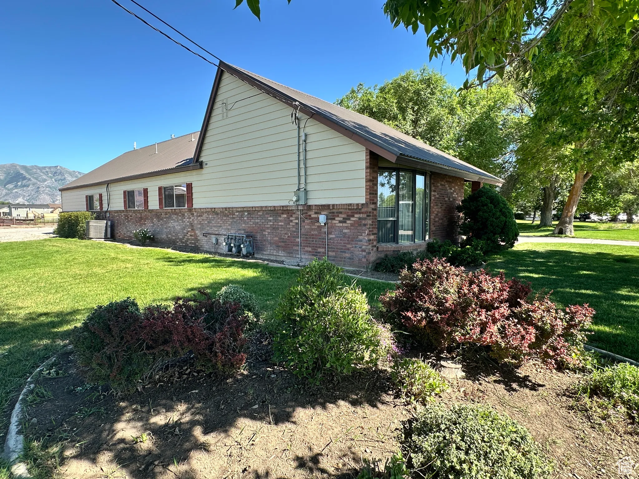 View of side of property featuring brick siding, a yard, central AC unit, and a mountain view