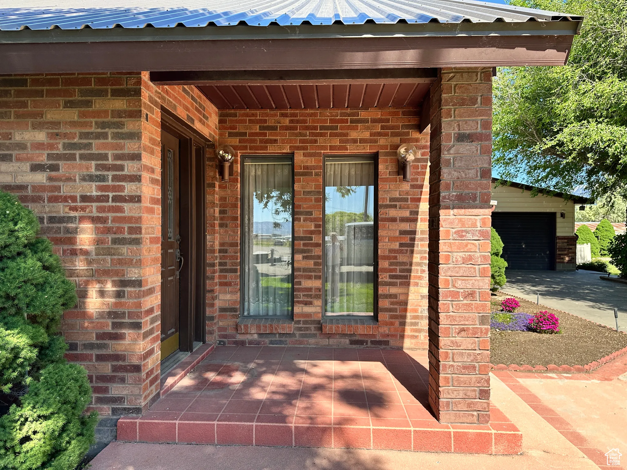 Doorway to property featuring brick siding, a garage, and metal roof