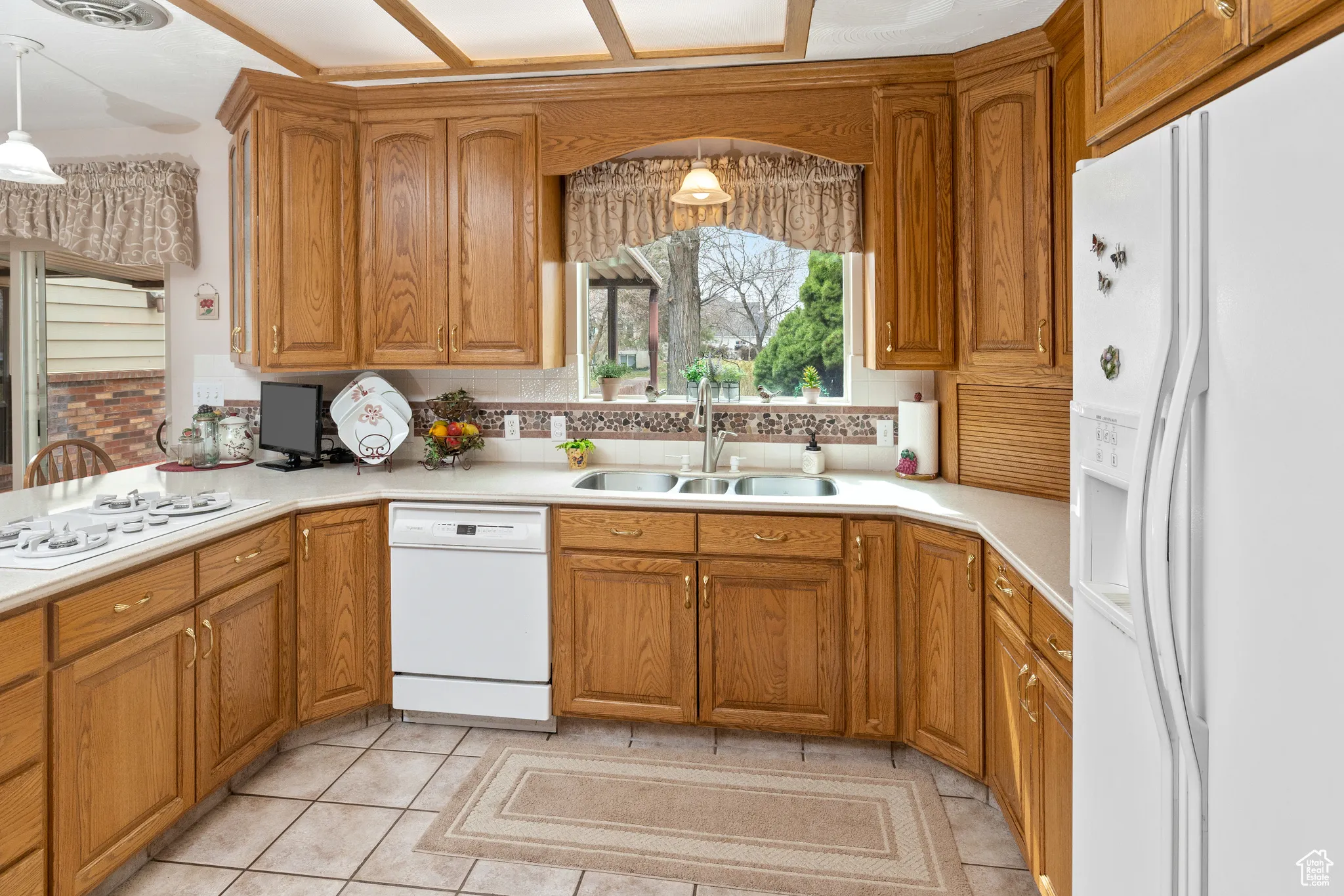 Kitchen featuring white appliances, a sink, tasteful backsplash, and brown cabinetry
