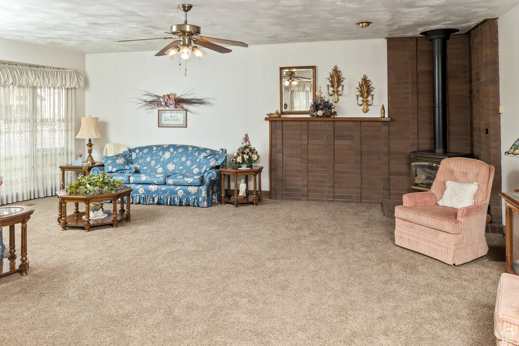 Carpeted living area with a ceiling fan, a wood stove, and a textured ceiling