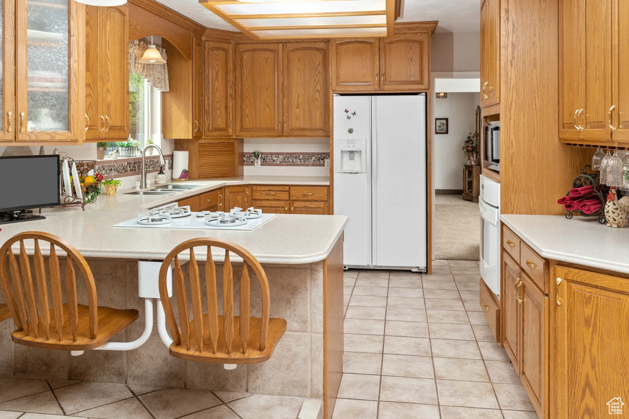 Kitchen with white appliances, a sink, light countertops, a peninsula, and glass insert cabinets