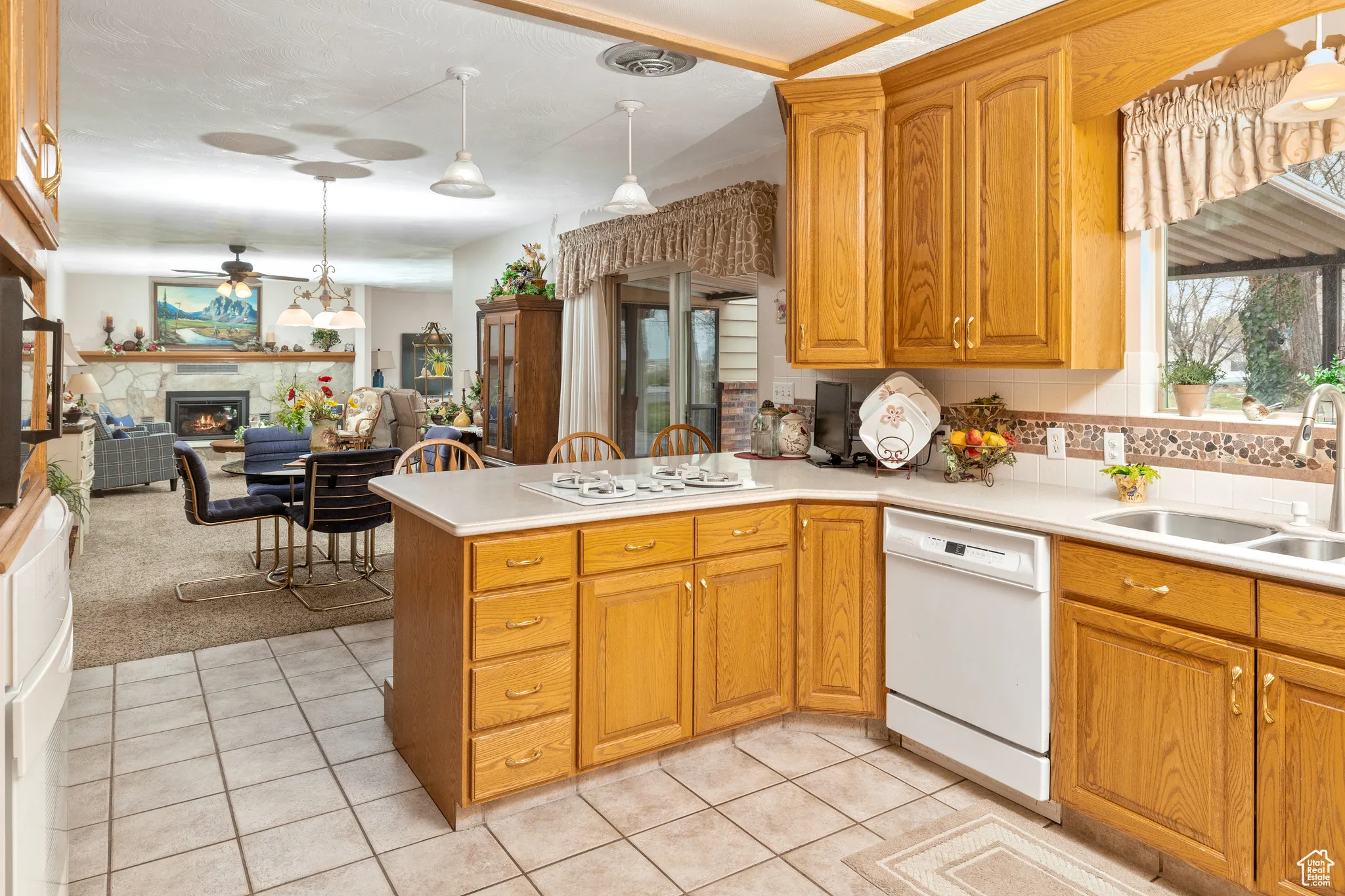 Kitchen with dishwasher, a sink, a ceiling fan, a warm lit fireplace, and a peninsula
