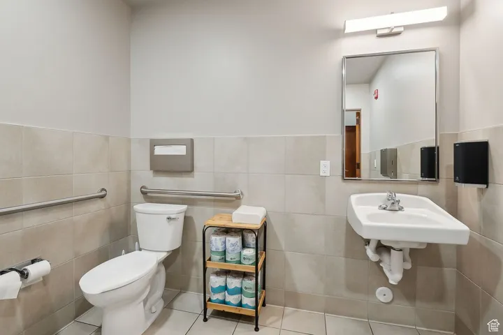 Half bath with toilet, tile patterned flooring, tile walls, wainscoting, and a sink