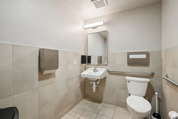 Bathroom featuring toilet, tile patterned floors, tile walls, and a wainscoted wall