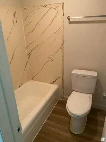 Full bathroom with wood finished floors, toilet, baseboards, and bathing tub / shower combination