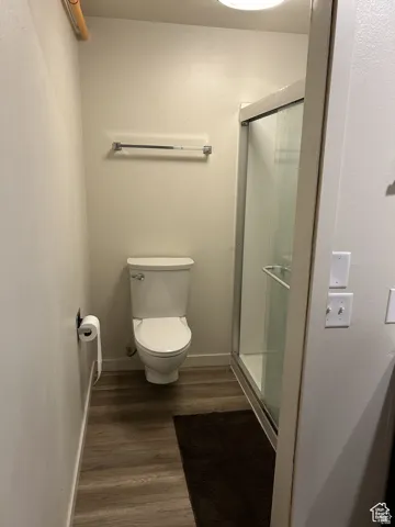 Full bathroom featuring wood finished floors, a shower stall, toilet, and baseboards