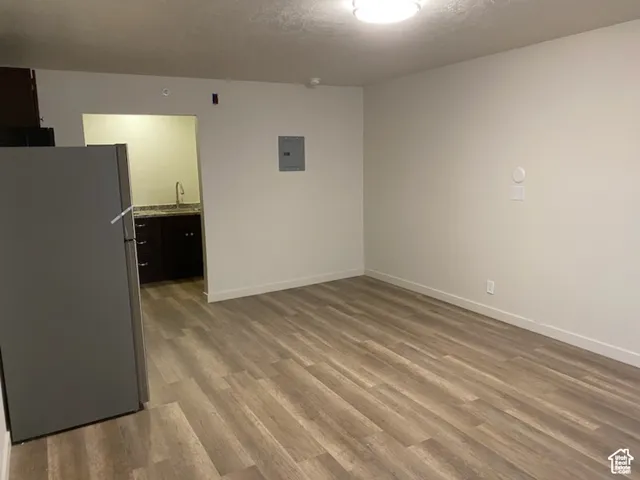 Empty room with a sink, light wood finished floors, electric panel, and baseboards