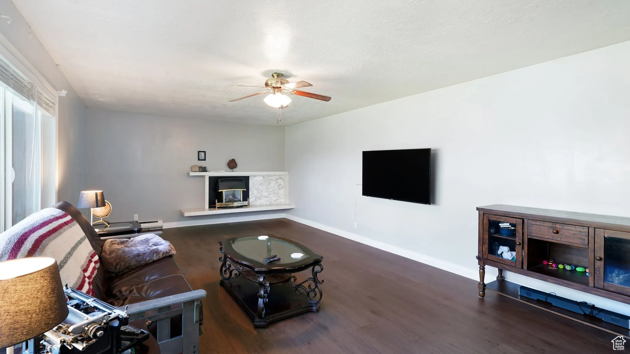 Living room with ceiling fan, wood finished floors, a glass covered fireplace, and baseboards