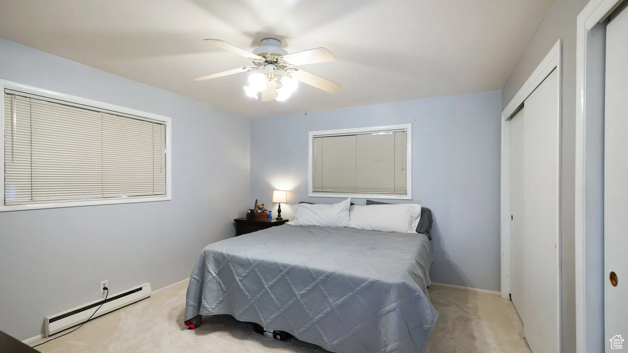 Carpeted bedroom featuring a baseboard radiator, a closet, baseboards, and a ceiling fan