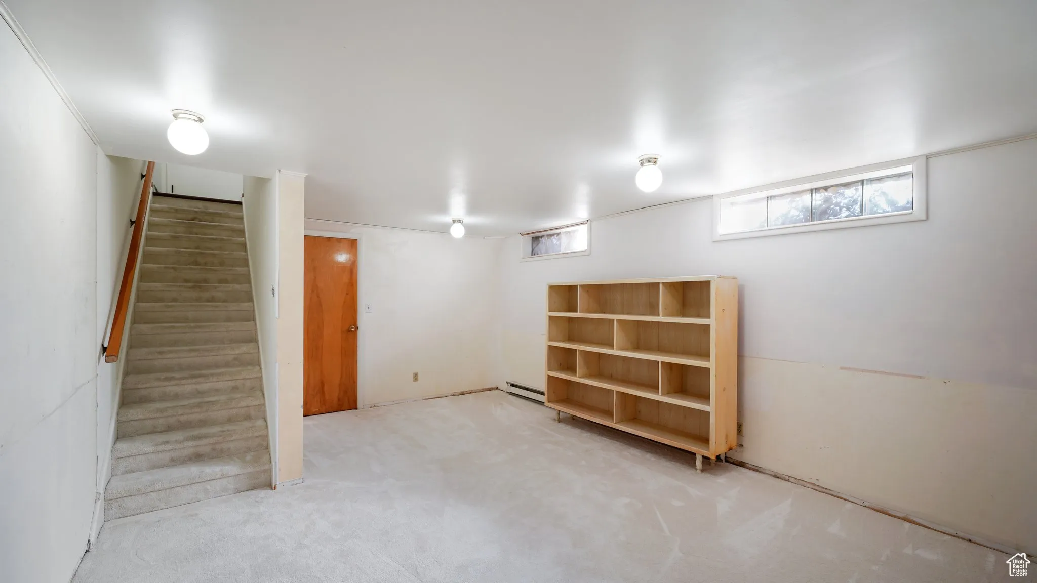 Basement featuring a baseboard heating unit, stairs, and carpet