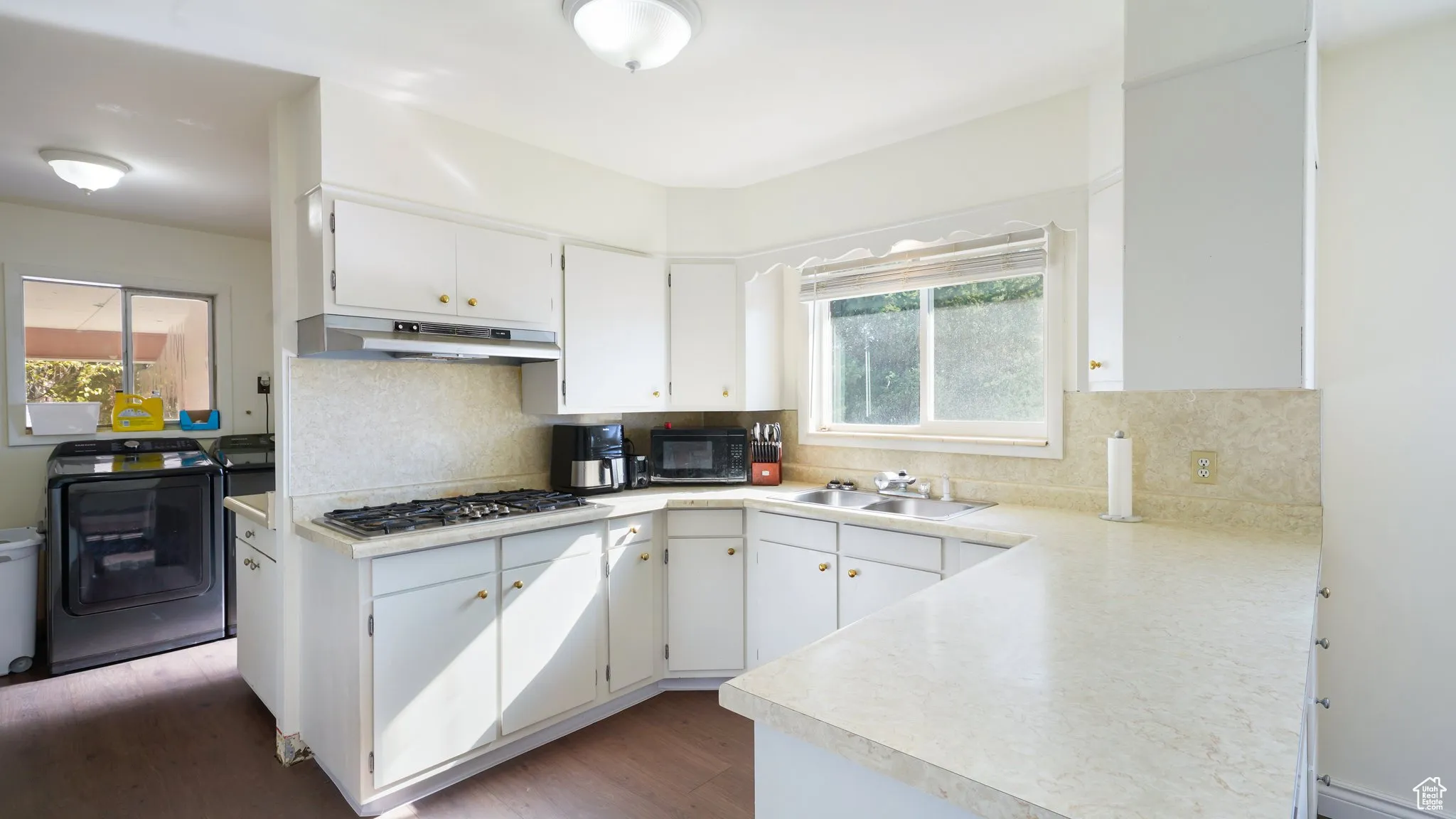 Kitchen featuring washer / clothes dryer, under cabinet range hood, a sink, stainless steel gas stovetop, and black microwave