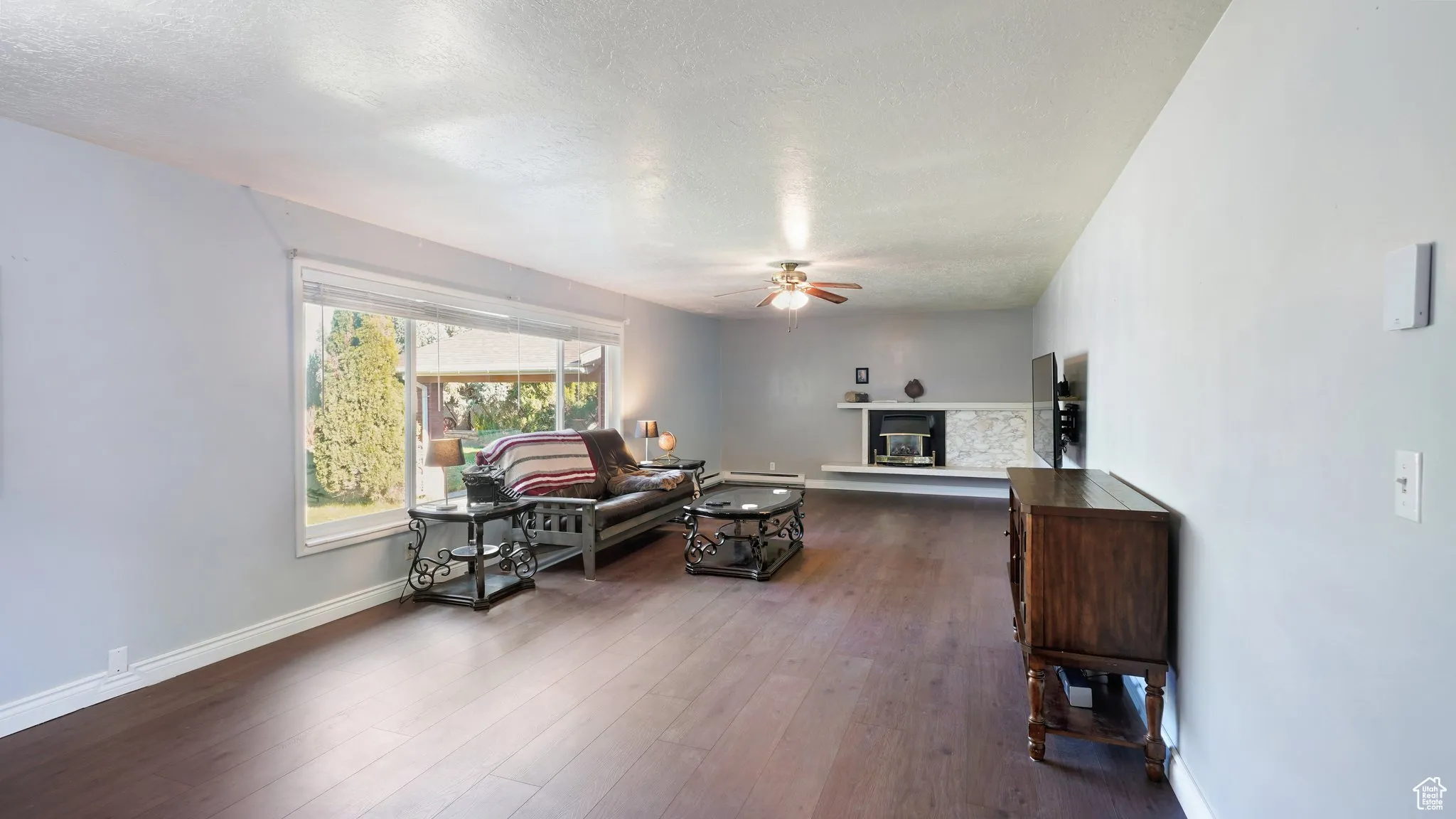 Living area with ceiling fan, a glass covered fireplace, a textured ceiling, dark wood-type flooring, and baseboards