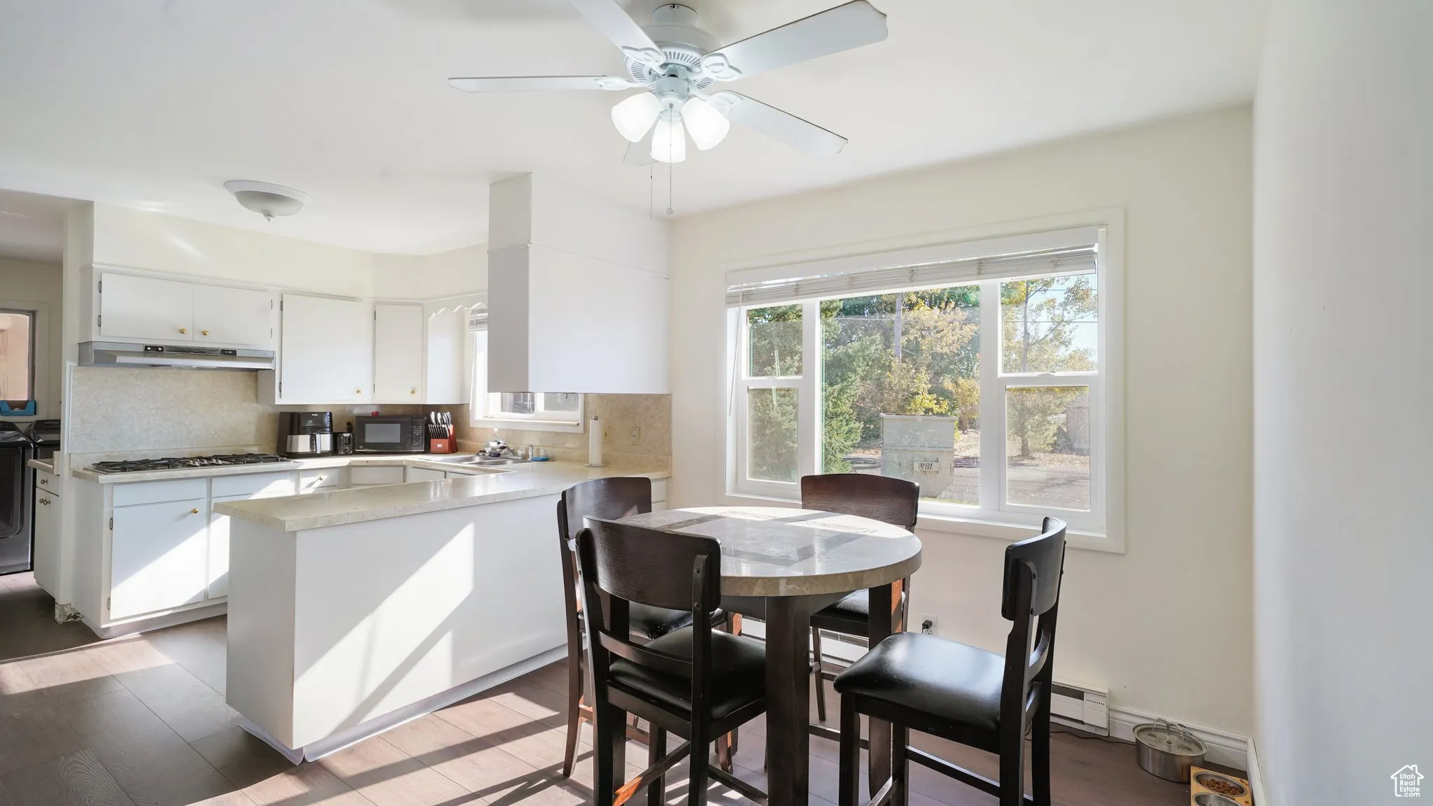 Kitchen with under cabinet range hood, black microwave, a peninsula, and tasteful backsplash