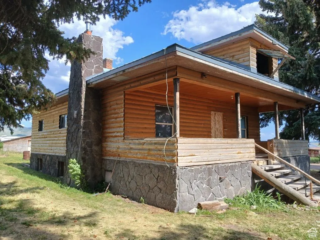 View of side of home featuring stairway, a chimney, and covered porch