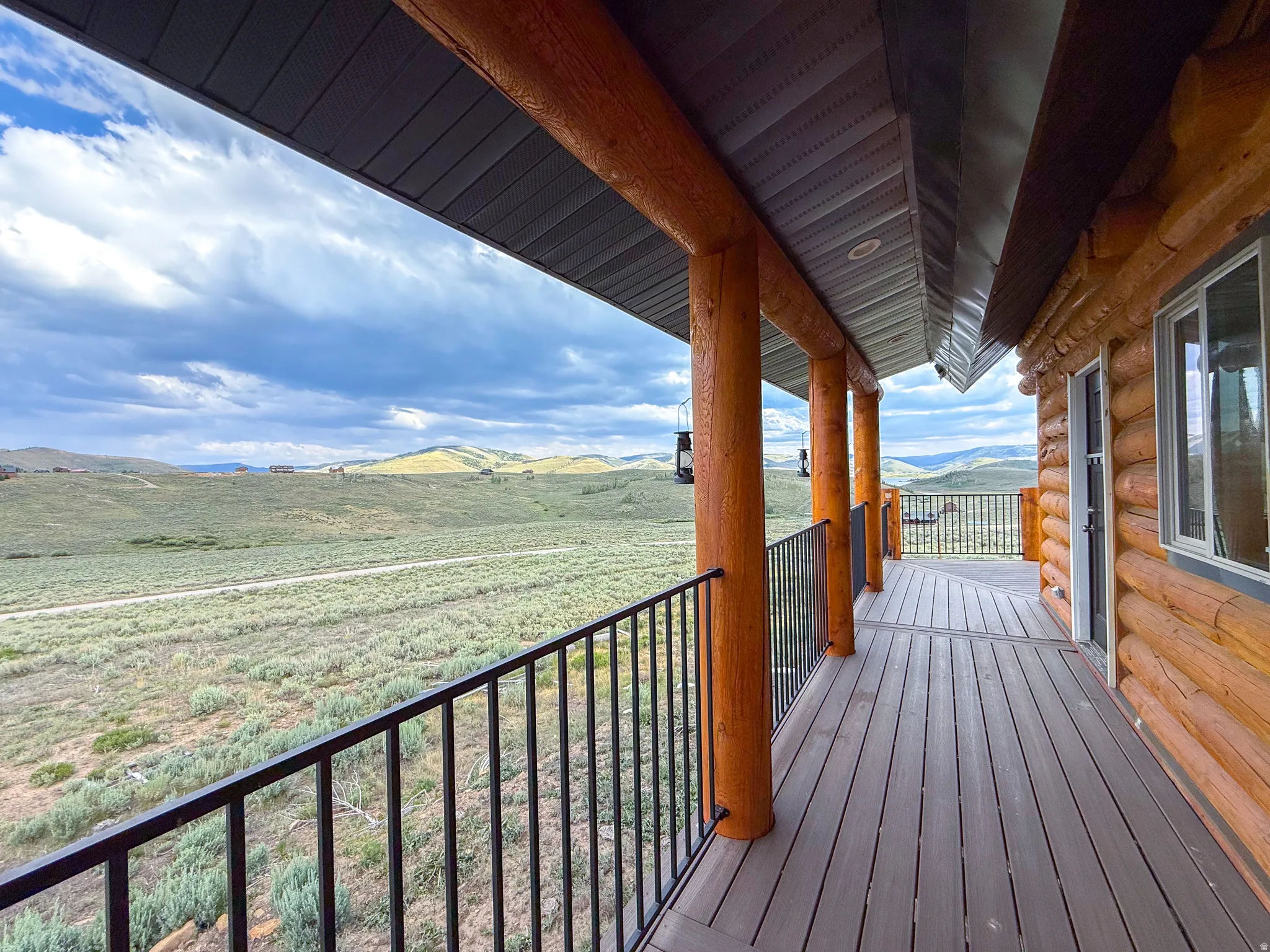 Covered deck featuring wood-finish flooring, log pillars, and black metal railings