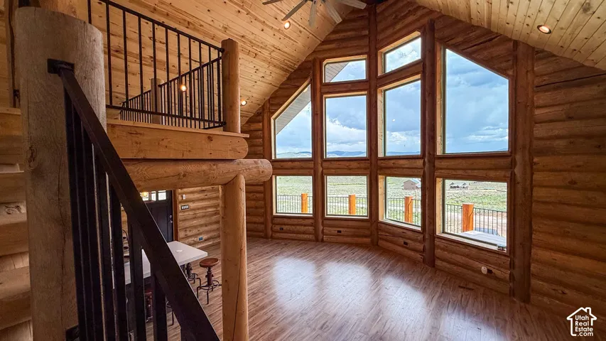 Living room featuring high vaulted ceiling, hardwood / wood-style floors, log walls, wood ceiling, and a ceiling fan