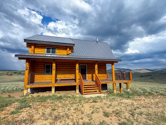 Log cabin exterior featuring a metal roof, an elevated porch with wood railings and black balusters, and an exterior staircase