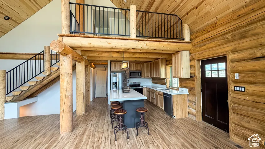 Kitchen featuring stainless steel appliances, a sink, high vaulted ceiling, light countertops, and rustic walls
