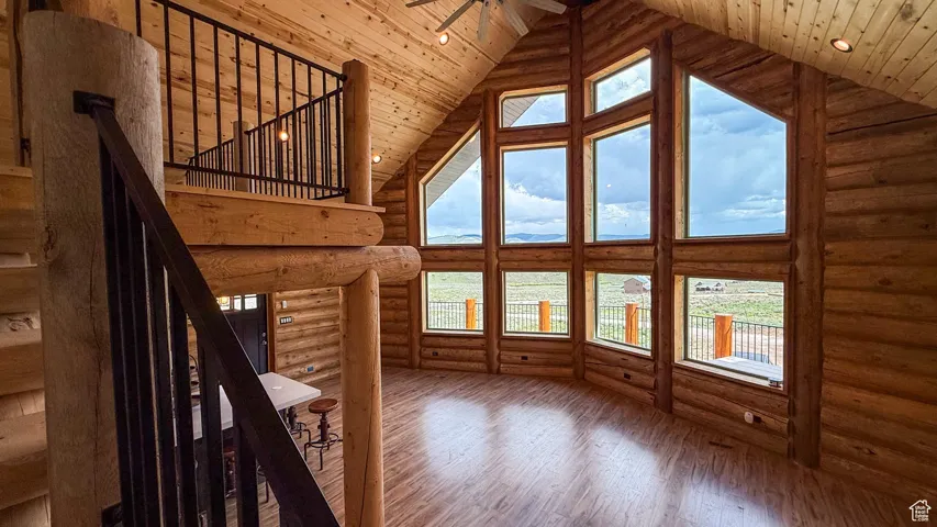 Living room featuring high vaulted ceiling, hardwood / wood-style floors, log walls, wood ceiling, and a ceiling fan