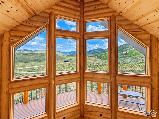 Natural wood-finish walls and vaulted ceiling, expansive window array, wood-finish deck with metal railing, and panoramic landscape