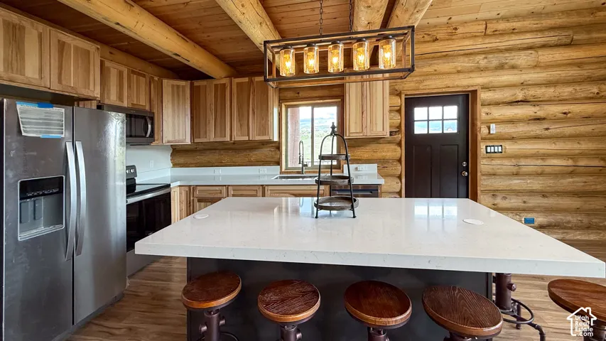 Kitchen featuring stainless steel appliances, log walls, wood ceiling with exposed beams, a sink, and light countertops