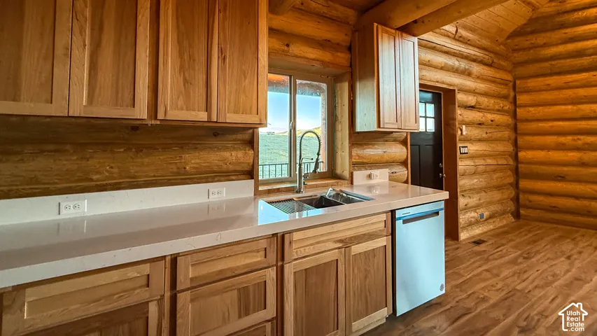 Kitchen with dark wood finished floors, log walls, light countertops, dishwasher, and beamed ceiling