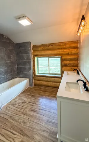 Full bath featuring log walls, double vanity, wood finished floors, lofted ceiling, and bathing tub / shower combination