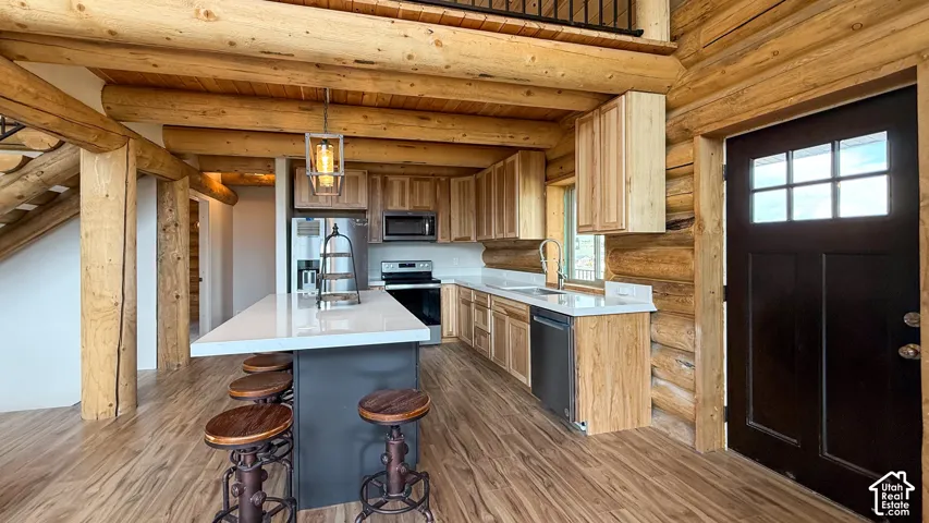 Kitchen featuring appliances with stainless steel finishes, log walls, dark wood-style flooring, light countertops, and wooden ceiling with exposed beams
