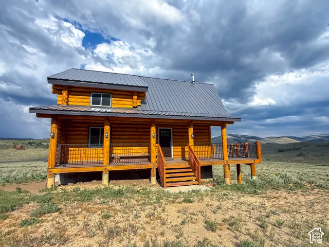 Log cabin exterior featuring a metal roof, an elevated porch with wood railings and black balusters, and an exterior staircase