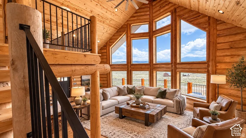 Soaring vaulted ceiling with exposed wood beams, extensive natural wood log construction, multi-pane windows, and a loft with wrought iron railing
