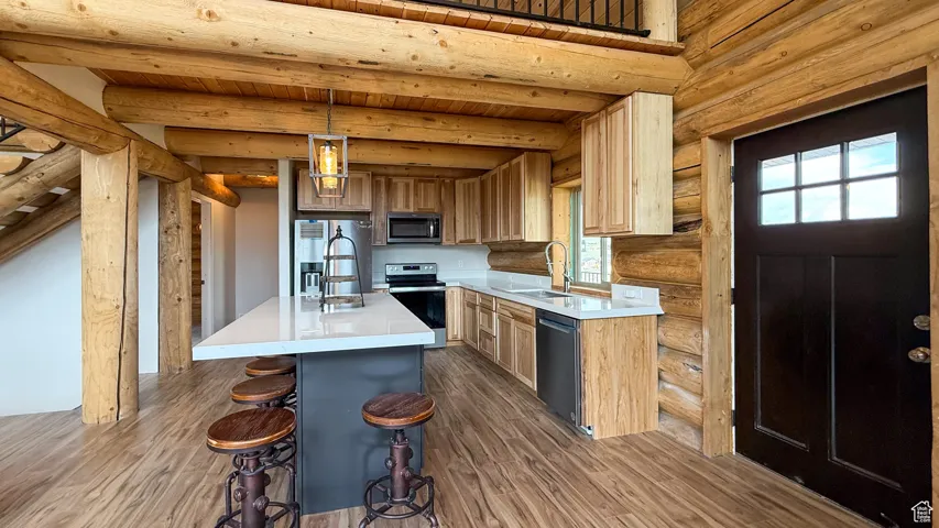 Kitchen featuring appliances with stainless steel finishes, log walls, dark wood-style flooring, light countertops, and wooden ceiling with exposed beams